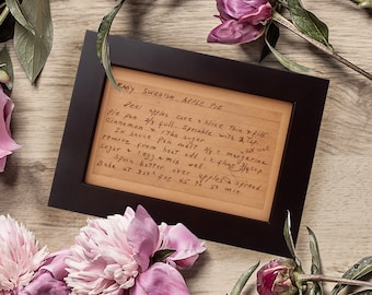 Op de afbeelding: Een ingelijst handgeschreven recept voor een gemakkelijke Zweedse appeltaart. Het recept is geschreven op gestreept papier met bruine inkt. De lijst is zwart en de achtergrond is een licht houten oppervlak.