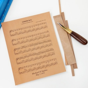 Photograph depicting the meticulous hand-cutting process of leather sheet music to fit the frame size. Prior to cutting, the wedding song was engraved on the leather with personalized details.