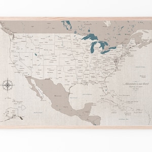 A framed, detailed USA map on 100 percent cotton canvas. The map is detailed with cities, states and capitols marked and labeled. It is on a natural cotton finish in shades of tan and beige with blue lakes and water detail. Personalized with names.