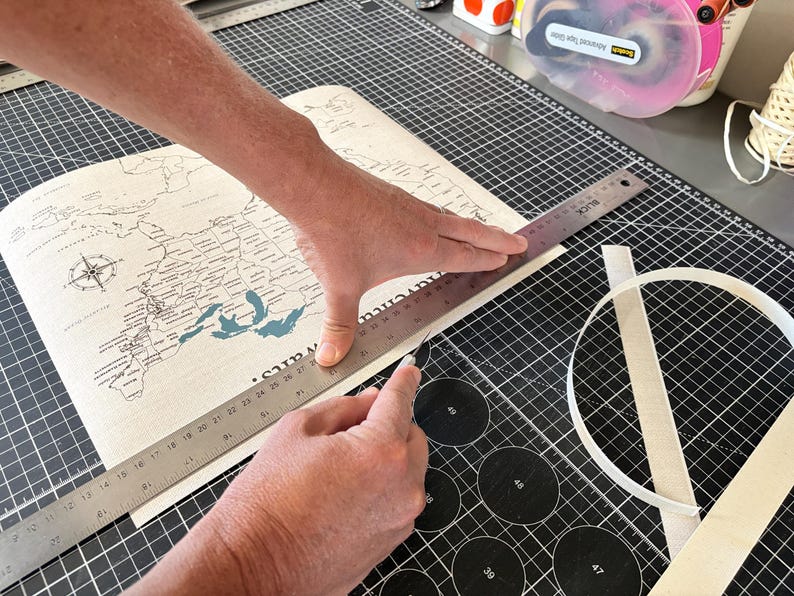 Behind the scenes at JW Design Studio Gifts: Jessica and Mike cut a custom 11x14 USA push pin travel map printed on cotton canvas, preparing each personalized map for framing and shipment in their home studio.