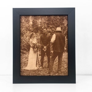 A wedding ceremony photo laser engraved on leather and framed in a dark walnut frame. The photo is an outdoor wedding, very casual and country setting. The leather photo has a warm sepia tone.