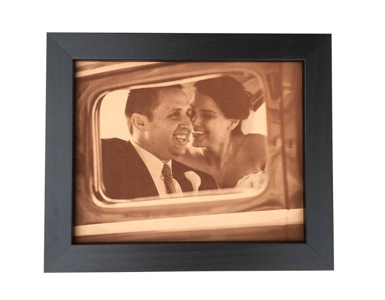 A leather photo of a wedding day celebration of a couple in a vintage car window. The leather photo is a warm sepia tone with rustic old fashioned look to it. The frame is a dark walnut frame.