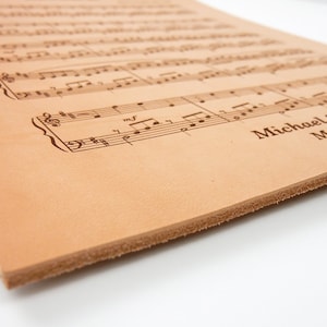 Detailed close-up of the engraved sheet music leather anniversary gift, capturing the real leathers thickness and the intricate engraving from a unique angle.