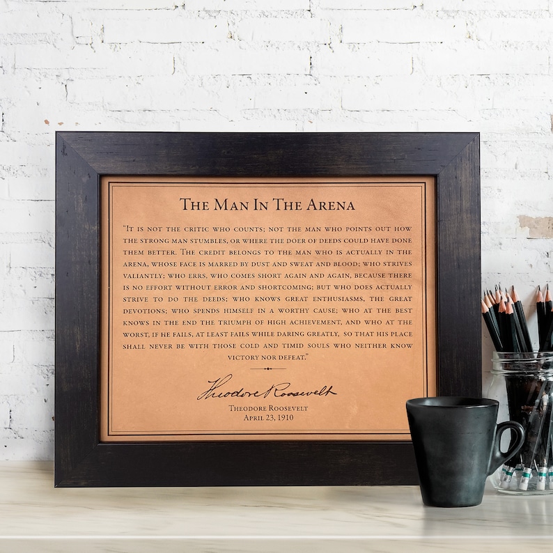 The Man in the Arena quote by Theodore Roosevelt laser engraved on genuine leather, framed in a dark walnut frame and displayed on a home or office desk. Inspirational wall art and luxury leather gift for men, perfect for graduation, lawyer gifts, office decor, promotions, or milestone achievements. Eco-friendly and sustainably sourced leather engraving for a timeless motivational keepsake that celebrates courage, resilience, and striving for success.