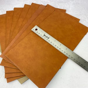 May include: A stack of ten brown leather sheets, each measuring 12 inches by 12 inches, with a ruler placed on top for scale.