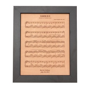 Personalized leather-engraved sheet music elegantly framed in dark walnut. Featuring a beloved wedding ceremony song with the couple's first names and wedding date.