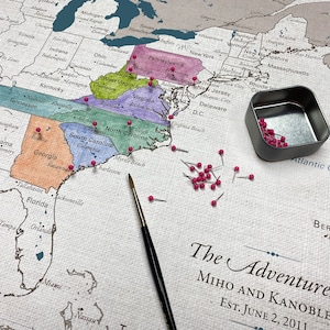 A do it yourself watercolor push pin travel map is printed on 100 percent cotton canvas with a neutral and natural cotton finish. Paint in the states visited and pin the exact cities for a unique travel keepsake. Personalized with names and date.