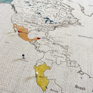 Sample image shows countries watercolor painted in with pins and a special heart on a specific location. Each map is printed on 100 percent cotton canvas. Water resistant to allow watercolor paints.