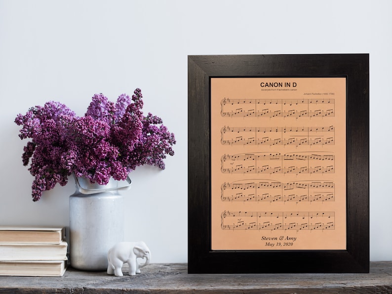 Personalized wedding song sheet music, beautifully engraved on leather and elegantly framed in dark walnut. This cherished keepsake includes the couple's first names and wedding date. The leather art rests on a desk adorned with purple flowers.