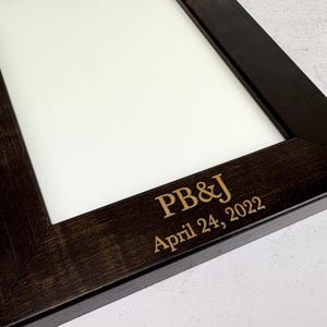 May include: A dark brown wooden picture frame with a white mat and the text "PB&J April 24, 2022" engraved on the bottom.