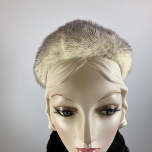 Peut inclure: Un chapeau de fourrure vintage aux tons gris clair et crème. Le chapeau est présenté sur une tête de mannequin, complété par une écharpe en fourrure noire. La fourrure du chapeau semble douce et moelleuse, offrant un look classique et élégant.