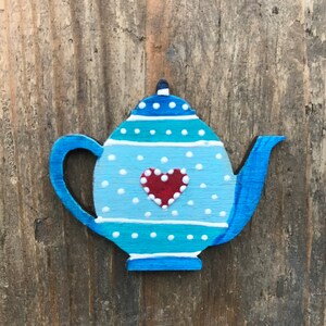 May include: A blue and white teapot with a red heart painted on the front. The teapot is decorated with white polka dots and blue stripes.