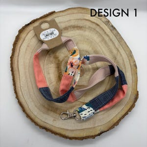 May include: A pink, blue and white patterned lanyard with a silver clasp. The lanyard has the text "Lanyard" printed on a tag.