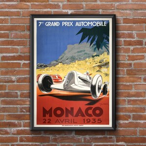 May include: A vintage poster advertising the 7th Grand Prix Automobile de Monaco, held on April 22, 1935. The poster features a white race car speeding through a winding road with a view of the city of Monaco in the background. The poster is framed in black.