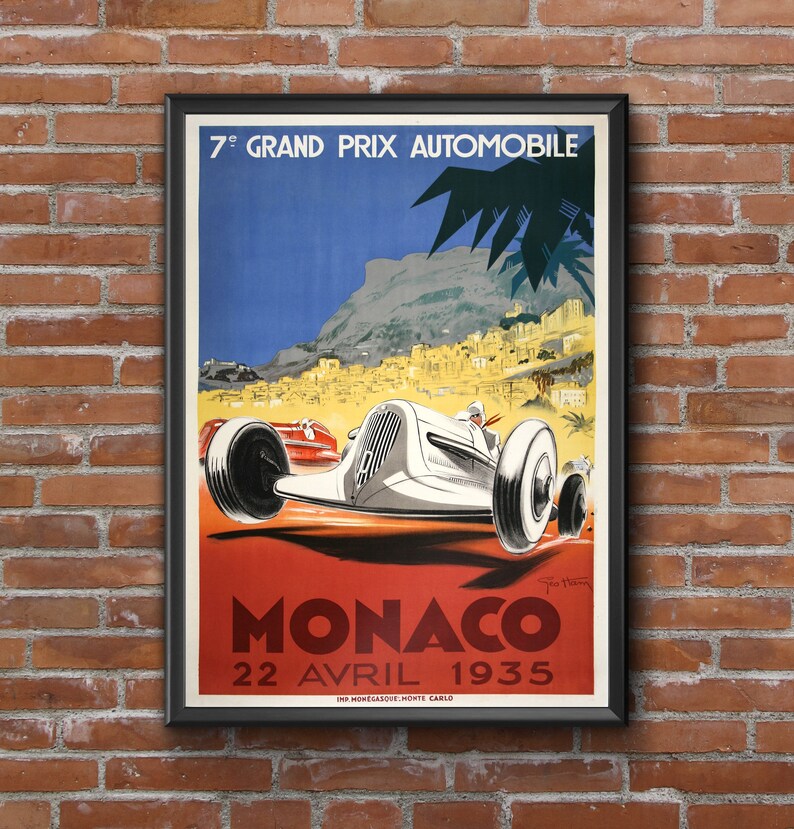 May include: A vintage poster advertising the 7th Grand Prix Automobile de Monaco, held on April 22, 1935. The poster features a white race car speeding through a winding road with a view of the city of Monaco in the background. The poster is framed in black.