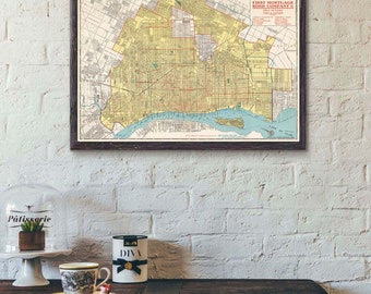 May include: A framed vintage map of Detroit, Michigan, with the title "Federal Detroit First Mortgage Bond Company" printed in the top right corner. The map is hanging on a white brick wall above a wooden table with a coffee cup and a small decorative tin.