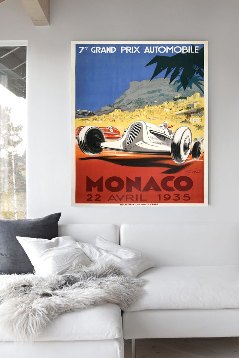 May include: Vintage poster advertising the 7th Grand Prix Automobile de Monaco, held on April 22, 1935. The poster features a white race car speeding through a winding road with a backdrop of the city of Monaco and the Mediterranean Sea.