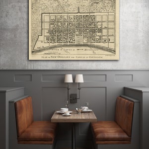 May include: A vintage map of New Orleans, Louisiana, showing the city's layout and streets. The map is printed on a cream-colored paper and framed in a black frame. The map is hanging on a gray wall.