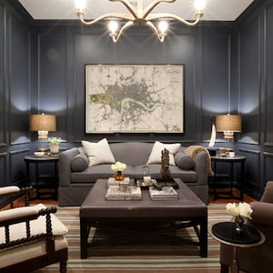 May include: A dark blue living room with a gray sofa, two armchairs, a coffee table, and a map of London on the wall. The room is decorated with lamps, plants, and throw pillows.