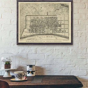 May include: A vintage black and white map of New Orleans, Louisiana, framed in a dark wood frame. The map shows the city's layout with streets and buildings, and includes the text "PLAN of NEW ORLEANS the CAPITAL of LOUISIANA."