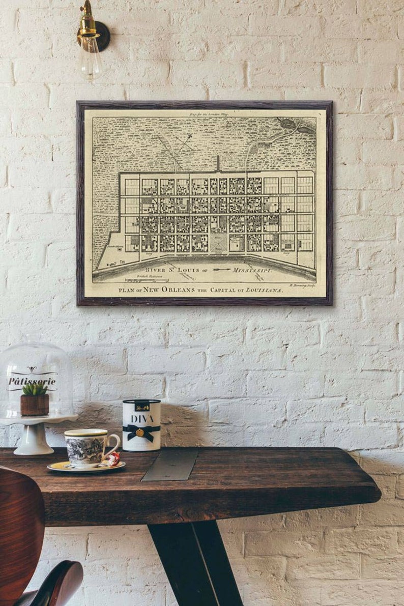 May include: A vintage black and white map of New Orleans, Louisiana, framed in a dark wood frame. The map shows the city's layout with streets and buildings, and includes the text "PLAN of NEW ORLEANS the CAPITAL of LOUISIANA."