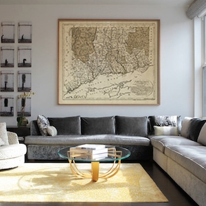 May include: A gray sectional sofa with multiple pillows sits in a living room with a glass coffee table and a framed map of New England on the wall.