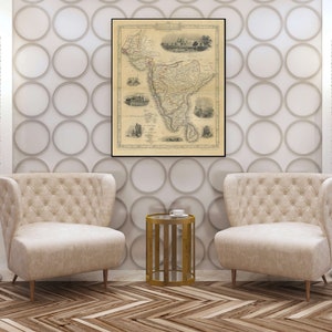 May include: Two beige armchairs with tufted upholstery and gold legs, facing each other in a living room setting. A gold metal side table with a glass top sits between the chairs. A vintage map of India hangs on the wall behind the chairs.