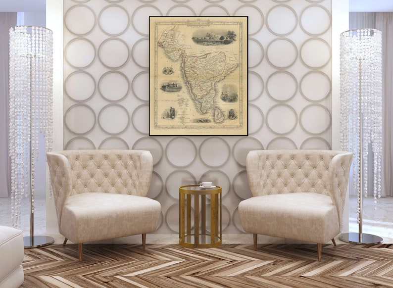 May include: Two beige armchairs with tufted upholstery and gold legs, facing each other in a living room setting. A gold metal side table with a glass top sits between the chairs. A vintage map of India hangs on the wall behind the chairs.