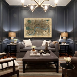 May include: A dark gray living room with a gray sofa, two armchairs, and a coffee table. The walls are decorated with a vintage map of London and framed black and white photographs. The room is lit by a chandelier and two lamps.