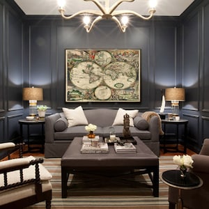 Puede incluir: Una sala de estar azul oscuro con un sof&aacute; gris, dos sillones y una mesa de caf&eacute;. La habitaci&oacute;n cuenta con una gran impresi&oacute;n de mapa del mundo antiguo en la pared, una l&aacute;mpara de ara&ntilde;a y dos l&aacute;mparas.