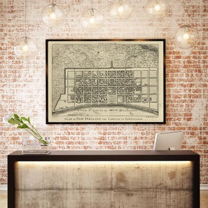 May include: A vintage map of New Orleans, Louisiana, framed in black, hangs on a brick wall above a modern, concrete reception desk with a black countertop and a built-in light.