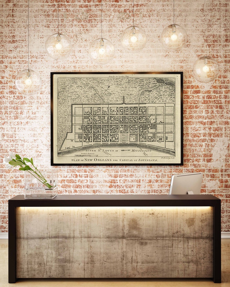 May include: A vintage map of New Orleans, Louisiana, framed in black, hangs on a brick wall above a modern, concrete reception desk with a black countertop and a built-in light.
