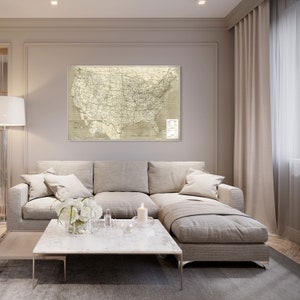Puede incluir: Un mapa vintage de los Estados Unidos de Am&eacute;rica cuelga en una pared sobre un sof&aacute; seccional beige con almohadas blancas. Una mesa de caf&eacute; de m&aacute;rmol blanco se encuentra frente al sof&aacute; con una vela blanca y flores blancas en un jarr&oacute;n.