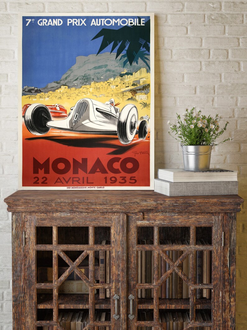 May include: Vintage poster advertising the 7th Grand Prix Automobile de Monaco, held on April 22, 1935. The poster features a white race car speeding through a winding road with a view of the city of Monaco in the background.