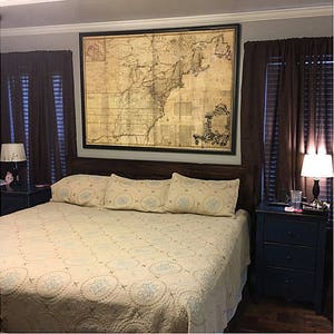 May include: A bedroom with a large framed map of the United States hanging above the headboard of a bed with a beige quilt and blue and white patterned pillows. There are two nightstands with lamps on either side of the bed.