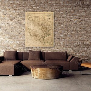 May include: An interior scene featuring a brown sectional sofa, a round wooden coffee table, and an orange chair with black metal legs. A vintage map of Texas hangs on the brick wall. A black floor lamp with a white shade is also present.