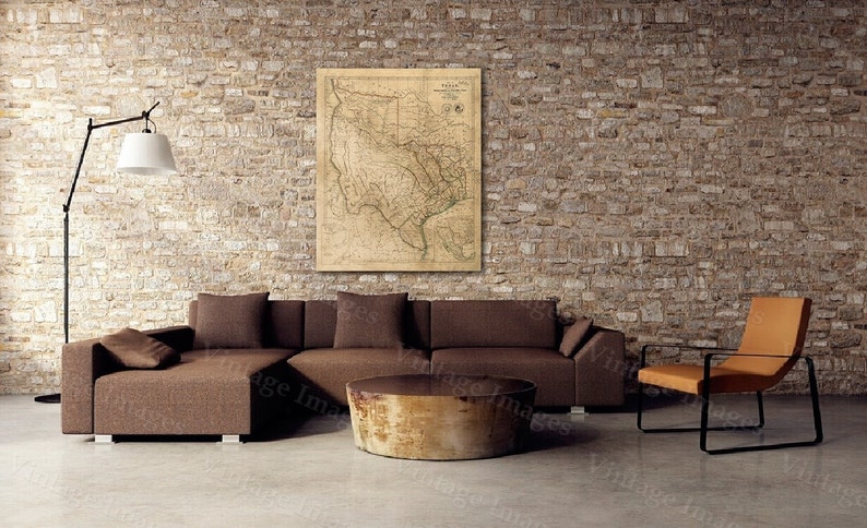 May include: An interior scene featuring a brown sectional sofa, a round wooden coffee table, and an orange chair with black metal legs. A vintage map of Texas hangs on the brick wall. A black floor lamp with a white shade is also present.