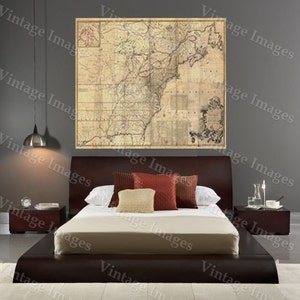 May include: A brown upholstered platform bed with a beige linen headboard and a white duvet. The bed is decorated with red and beige throw pillows. A vintage map of North America hangs on the wall behind the bed.