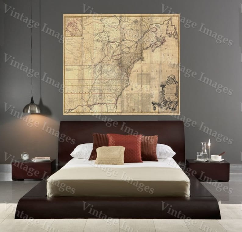 May include: A brown upholstered platform bed with a beige linen headboard and a white duvet. The bed is decorated with red and beige throw pillows. A vintage map of North America hangs on the wall behind the bed.