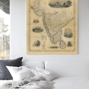 May include: An antique map of South America, printed in black and white with red and brown accents. The map is framed and hanging on a white wall above a white couch with gray pillows.