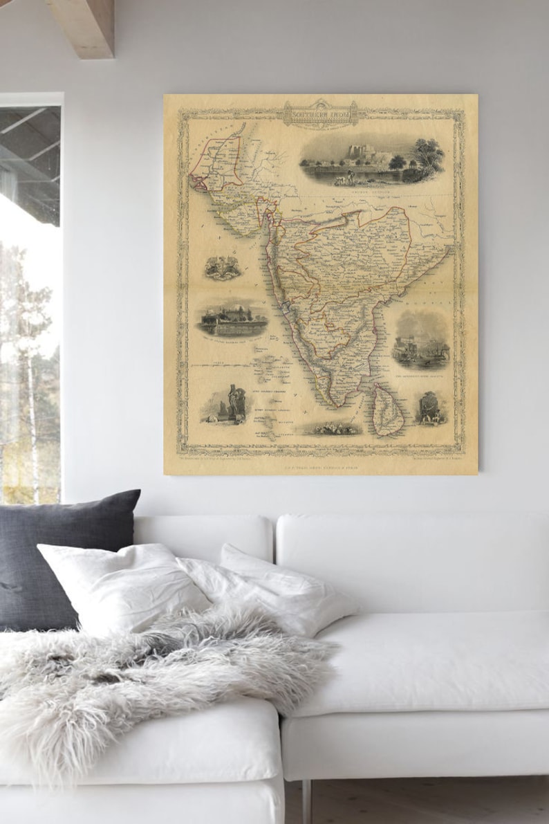 May include: An antique map of South America, printed in black and white with red and brown accents. The map is framed and hanging on a white wall above a white couch with gray pillows.