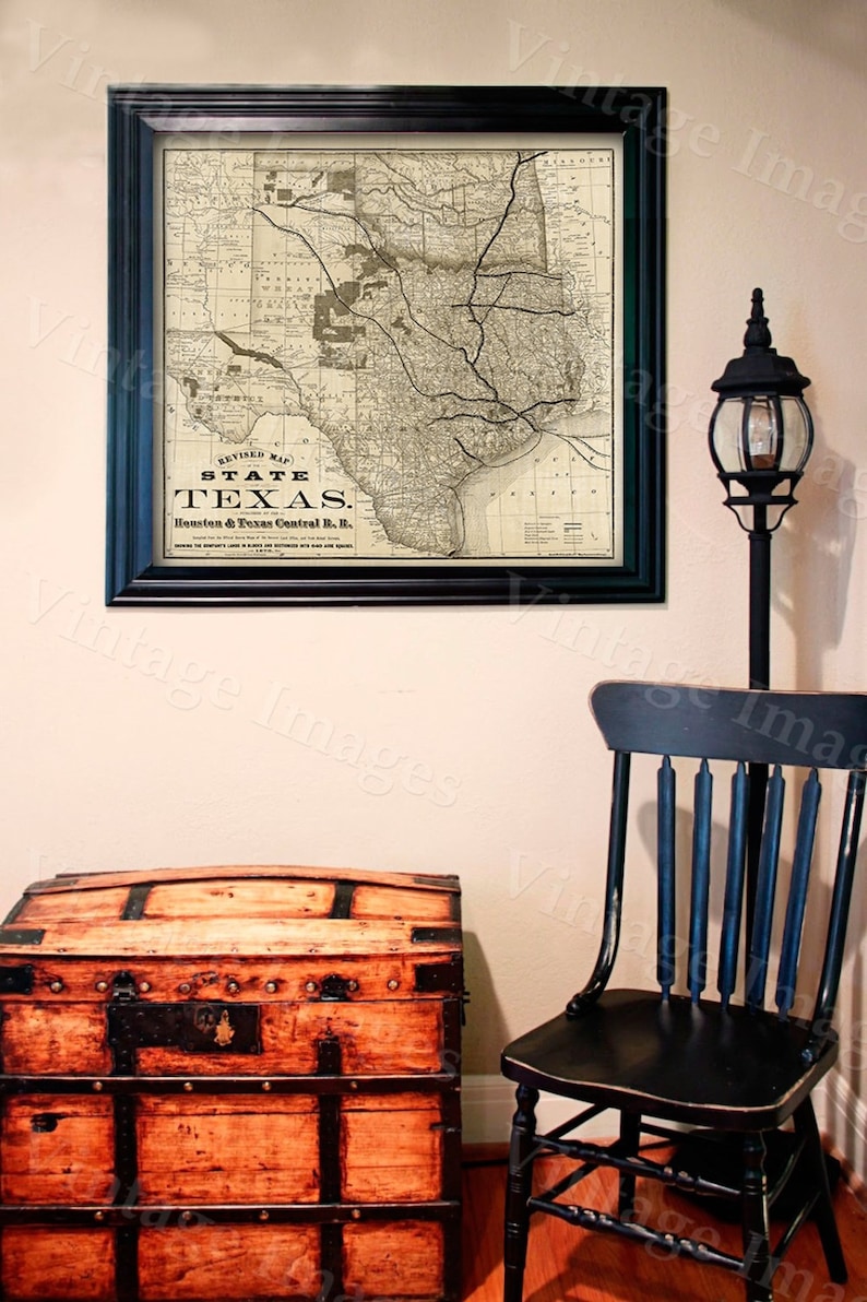 Pode incluir: Um mapa vintage emoldurado do estado do Texas, com o texto "REVISED MAP STATE TEXAS. Houston & Texas Central R.R." impresso no mapa. O mapa est&aacute; pendurado em uma parede com um ba&uacute; de madeira e uma cadeira preta em primeiro plano.
