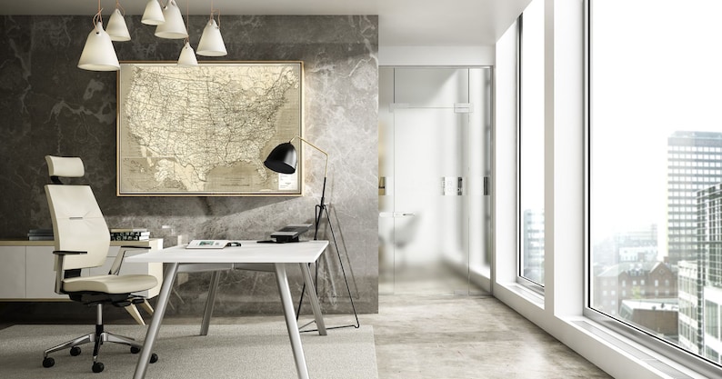 Puede incluir: Una silla de oficina blanca con reposacabezas y brazos ajustables, un escritorio blanco con una mesa blanca y patas de madera, una l&aacute;mpara negra con un soporte dorado y un mapa enmarcado de los Estados Unidos en una pared gris.