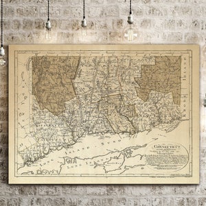 May include: An antique map of Connecticut, printed in black and white on a cream-colored paper. The map shows the state's counties and major towns, with a key in the lower right corner. The map is framed and hanging on a brick wall.