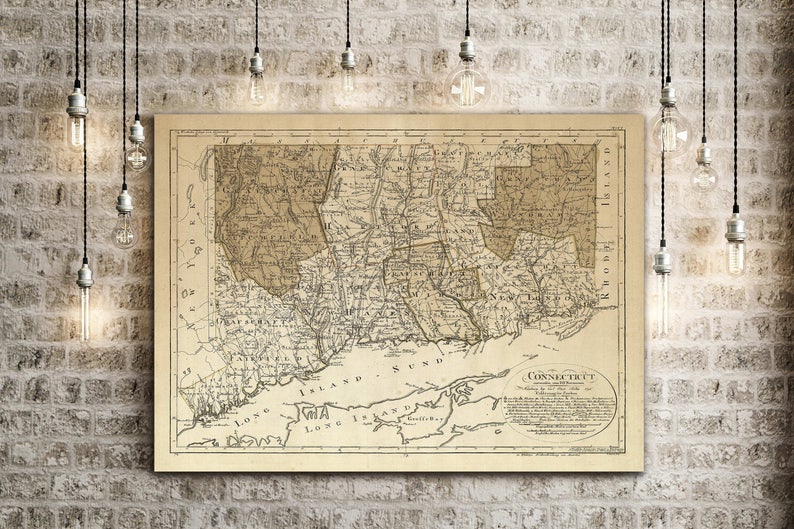 May include: An antique map of Connecticut, printed in black and white on a cream-colored paper. The map shows the state's counties and major towns, with a key in the lower right corner. The map is framed and hanging on a brick wall.
