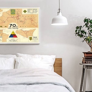 May include: A vintage map showing the combat operations of the 70th Tank Battalion during World War II. The map shows the battalion's movements across Europe and Sicily, with key locations and dates marked. The map is framed and displayed on a white wall.
