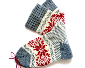 May include: A pair of gray and white knitted socks with a red snowflake pattern. The socks have a red string tie at the top.