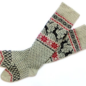 May include: A pair of beige knit socks with a festive pattern. The socks feature black reindeer and red snowflake designs on a dotted background. The cuffs and toes have red and black geometric patterns.
