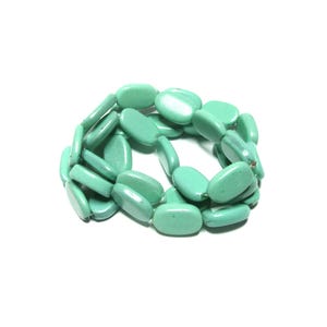 May include: A turquoise-colored bracelet composed of oval-shaped beads. The beads are strung together, forming a flexible band. The bracelet is set against a white background, highlighting its color and design. This accessory is suitable for everyday wear.
