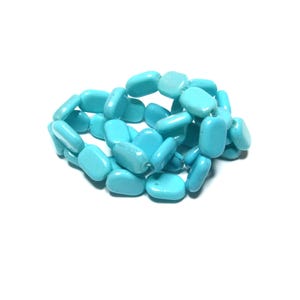 May include: A bracelet made of light blue, rectangular beads. The beads are strung together, forming a circular shape. The bracelet is set against a white background, highlighting the vibrant color of the beads.